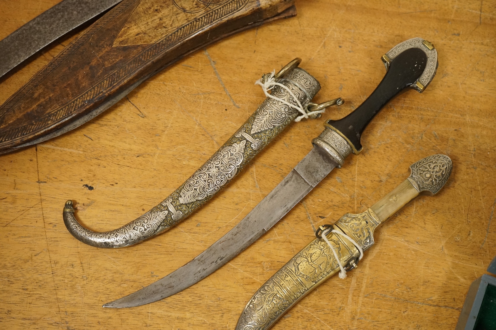 An Indian sword tulwar, the iron hilt with traces of chiselled and inlaid decoration, together with a kukri in its wooden scabbard, a Syrian jambya and a Moroccan jambiya (4)